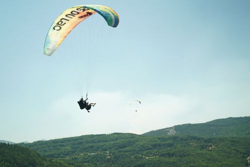 Free A paraglider enjoying a summer flight over lush green mountains under a clear sky. Stock Photo