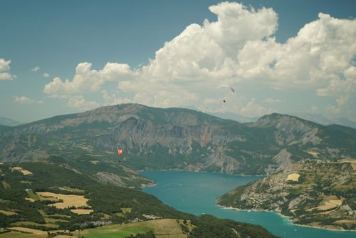 Free Captured paraglider soaring above a picturesque alpine lake with majestic mountains and clouds. Stock Photo