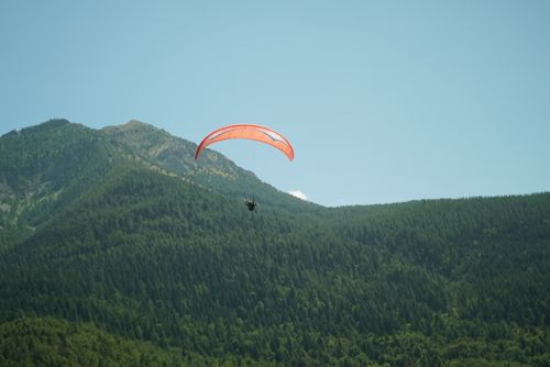 Free A lone paraglider flies over scenic green mountains under a clear blue sky in summer. Stock Photo