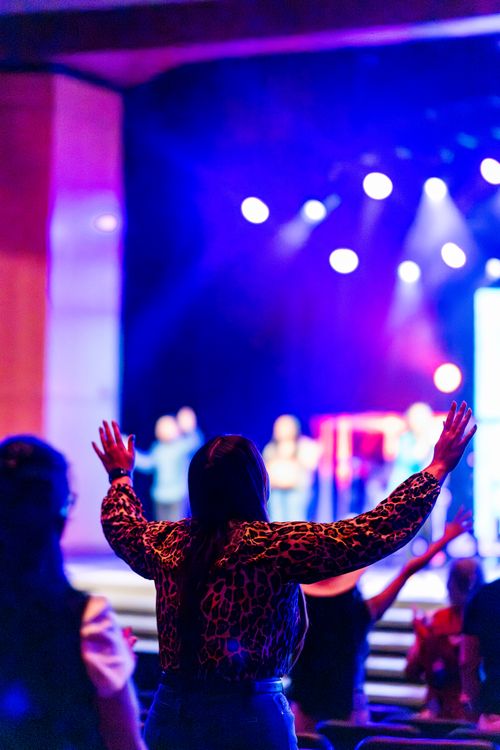 Free A woman raises her arms at a vibrant indoor concert, embracing the lively atmosphere. Stock Photo