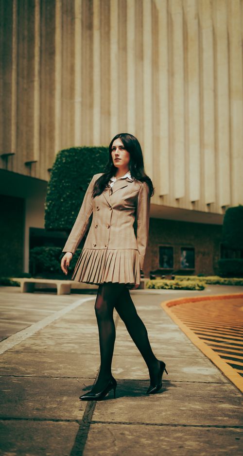 Free Stylish woman in a formal dress walking confidently by a modern building. Stock Photo