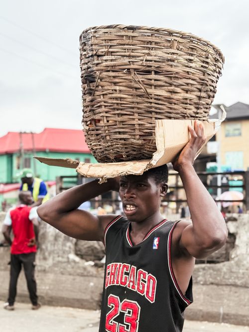 Free Young man carrying a basket in bustling Lagos market street, Nigeria. Stock Photo