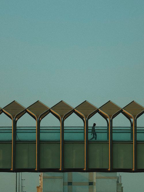 Free A lone figure walks across a geometric pedestrian bridge at dusk, showcasing modern architecture. Stock Photo