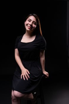 Smiling woman posing in a black dress against a dark studio background.