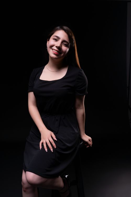 Free Smiling woman posing in a black dress against a dark studio background. Stock Photo