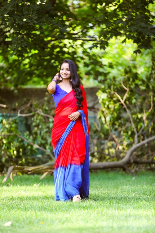 Free A woman in a vibrant red and blue saree walks gracefully on a sunny day outdoors. Stock Photo