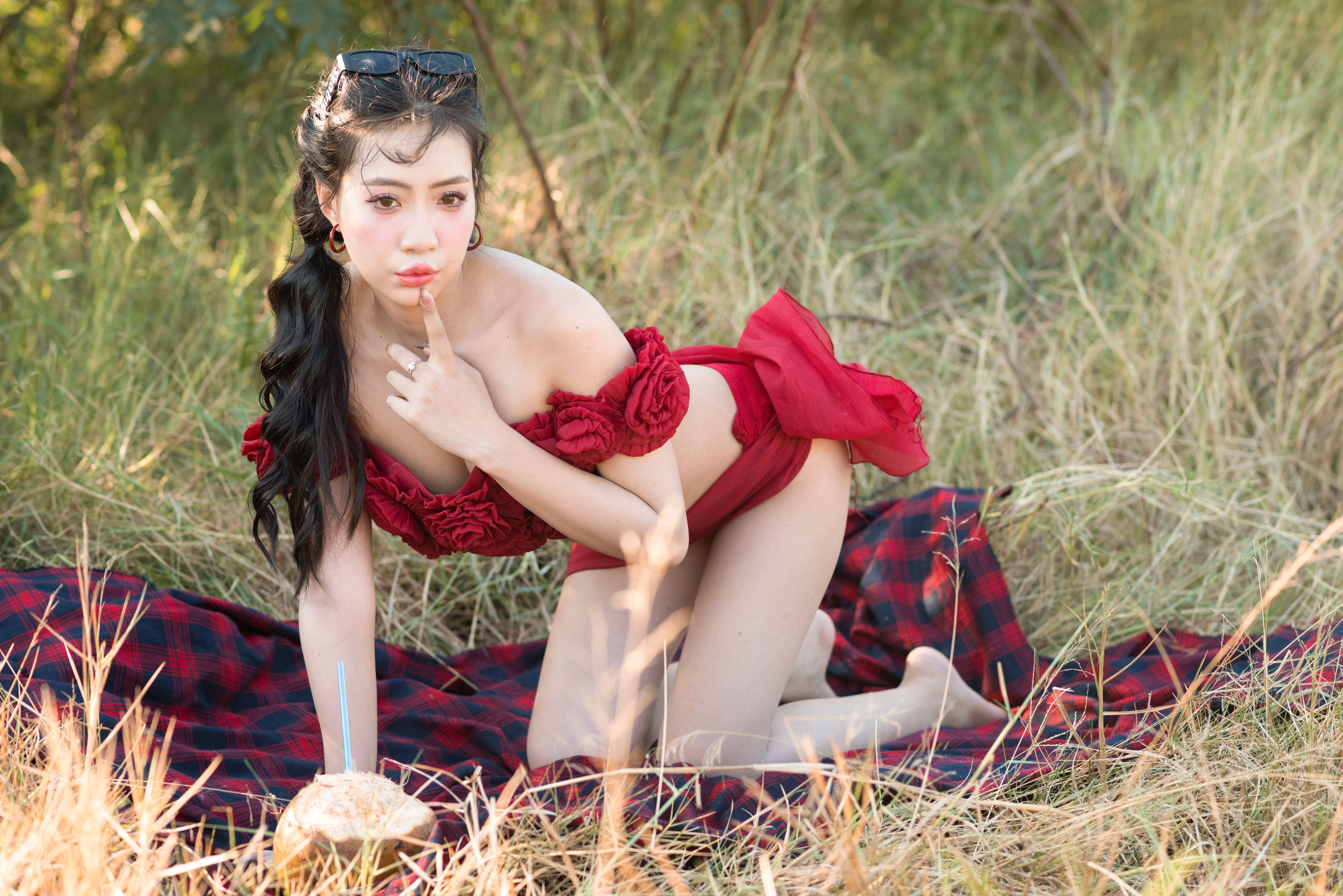 A woman in a red dress poses outdoors enjoying a picnic on a sunny day with coconut juice.
