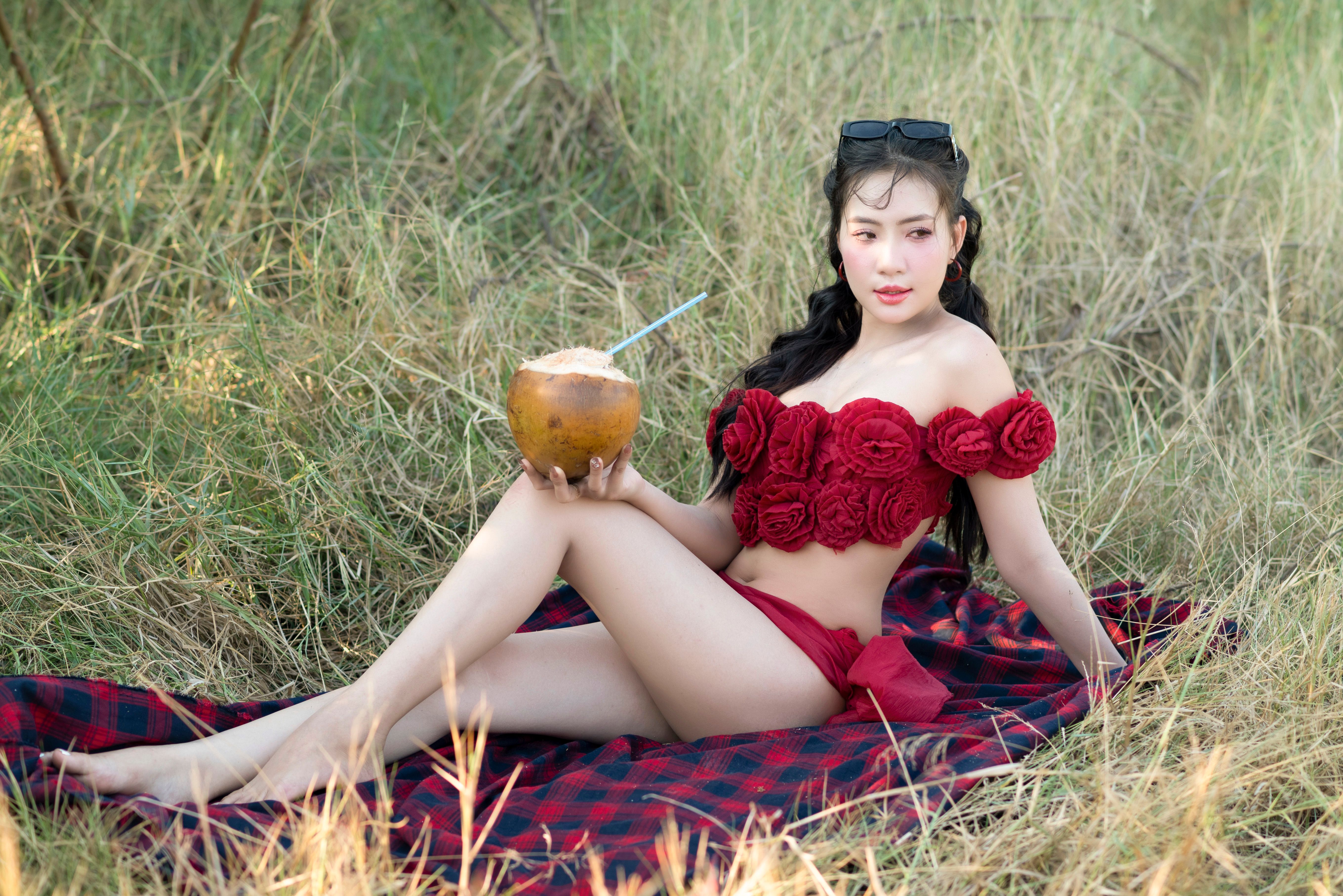 Woman in floral outfit enjoying coconut drink on a sunny day outdoors.