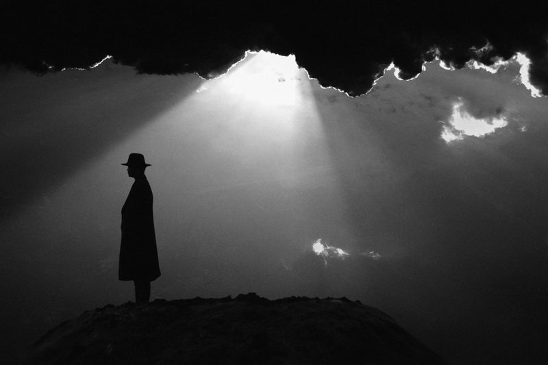 A silhouette of a man standing under dramatic clouds with light rays shining through., by Jay Satriani on Pexels