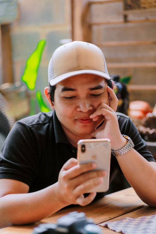 Free Young man wearing a cap interacting with his phone in a cozy indoor setting. Stock Photo