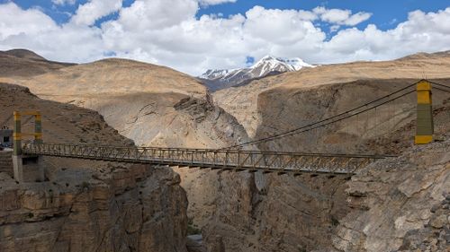 Free A suspension bridge spans a deep canyon with a snowy mountain in the background. Stock Photo