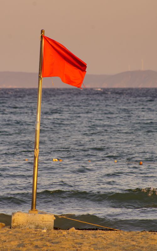 Free A vibrant red flag on the sandy shores of Şarköy, Tekirdağ, Türkiye, signals caution at twilight. Stock Photo