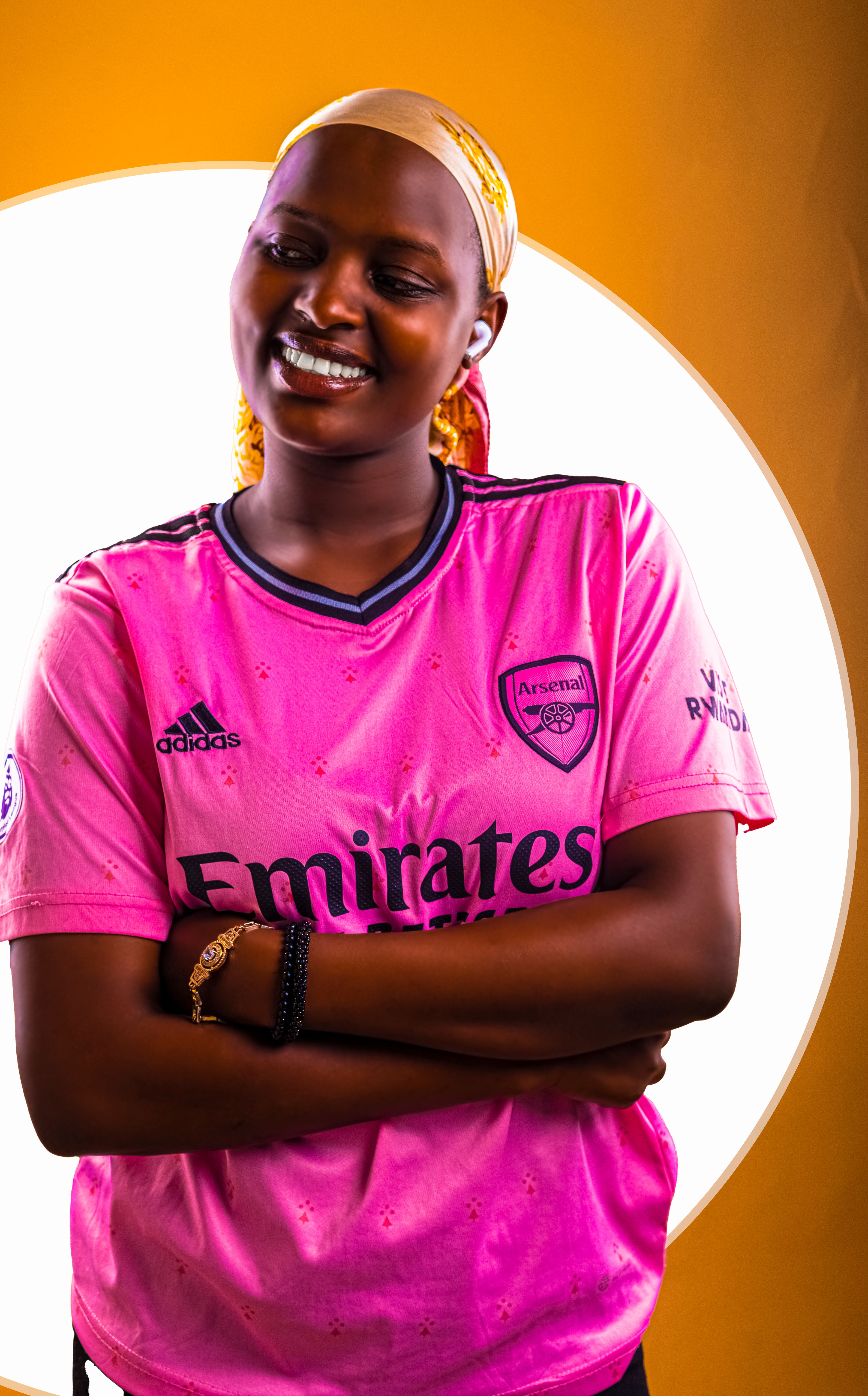 Cheerful woman posing in a pink Arsenal football jersey indoors.