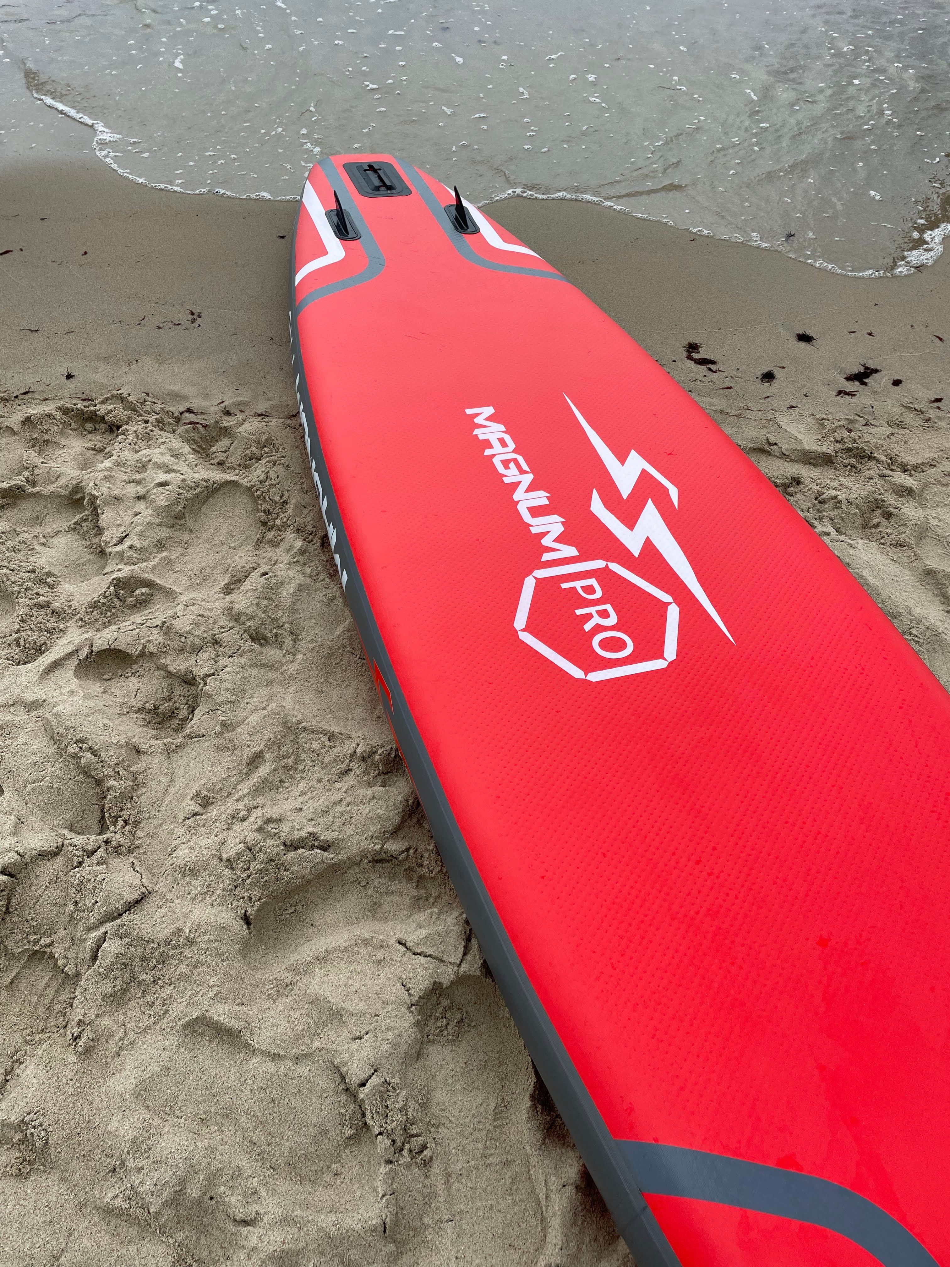 Close-up of a vibrant red Magnum Pro surfboard lying on a sandy beach shore in Russia.