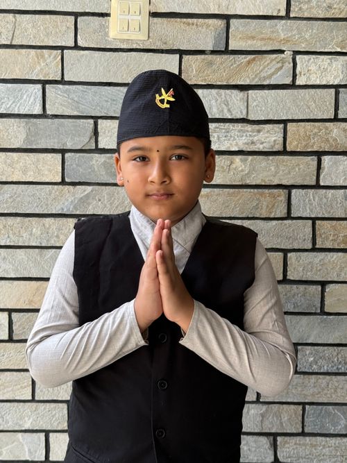 Free Young boy in traditional wear offering a respectful hand gesture against brick wall. Stock Photo