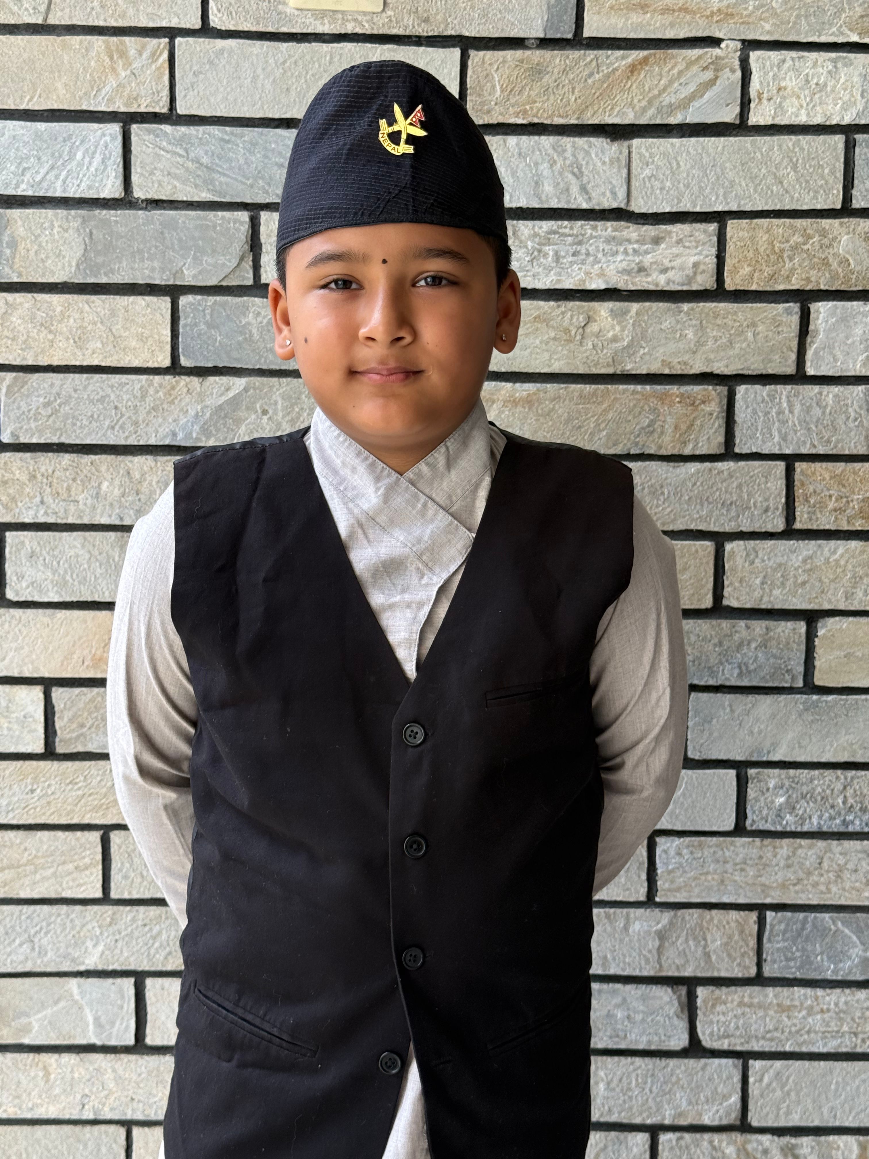 Young boy in traditional attire standing against a brick wall.