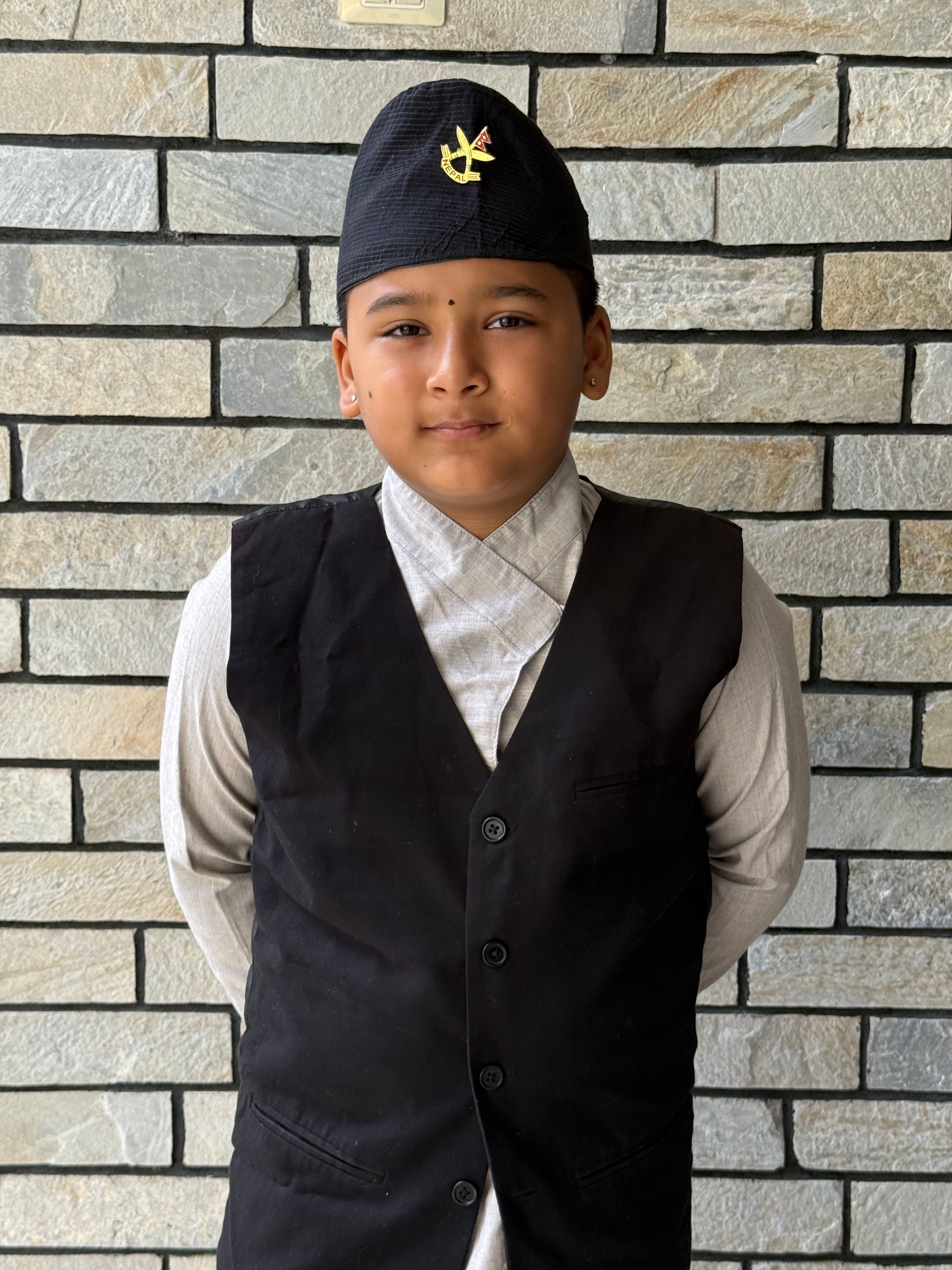 A young boy wearing traditional attire standing against a brick wall, exuding a charming demeanor.