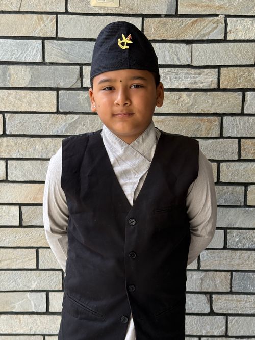 Free A young boy wearing traditional attire standing against a brick wall, exuding a charming demeanor. Stock Photo