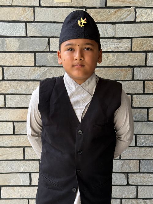 Free Young boy in traditional clothing against a brick wall, looking directly at the camera. Stock Photo