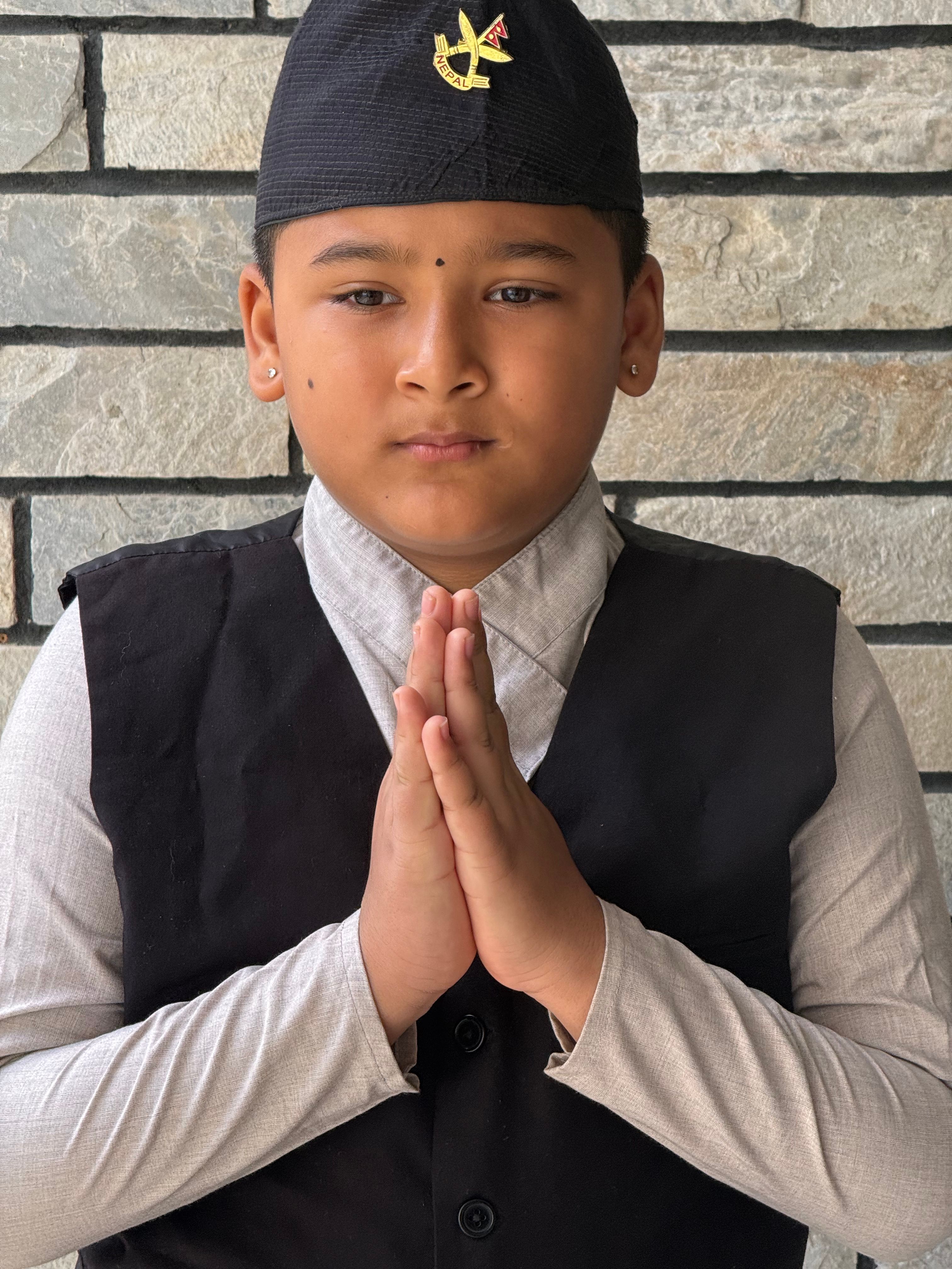 Portrait of a young boy in traditional clothing with hands in a prayer gesture.