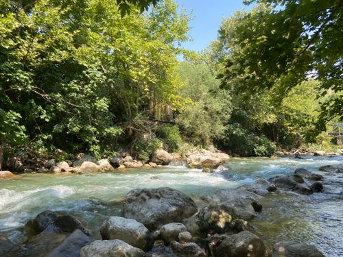 Free Beautiful river flowing amidst lush greenery and rocks in Muğla, Türkiye, under a clear blue sky. Stock Photo