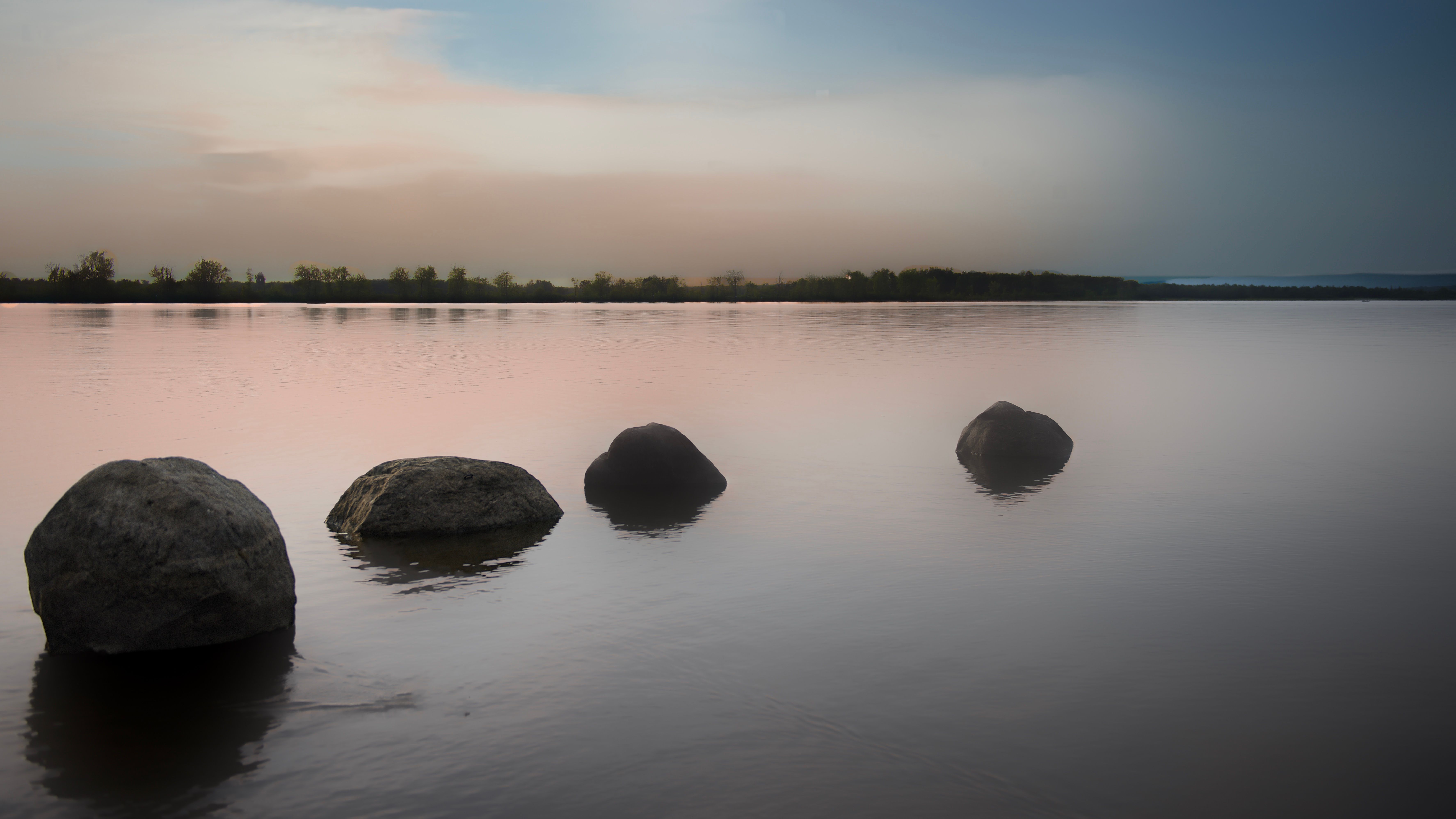 Tranquil lakeside scene with smooth rocks and a pastel sunset, reflecting calmness.