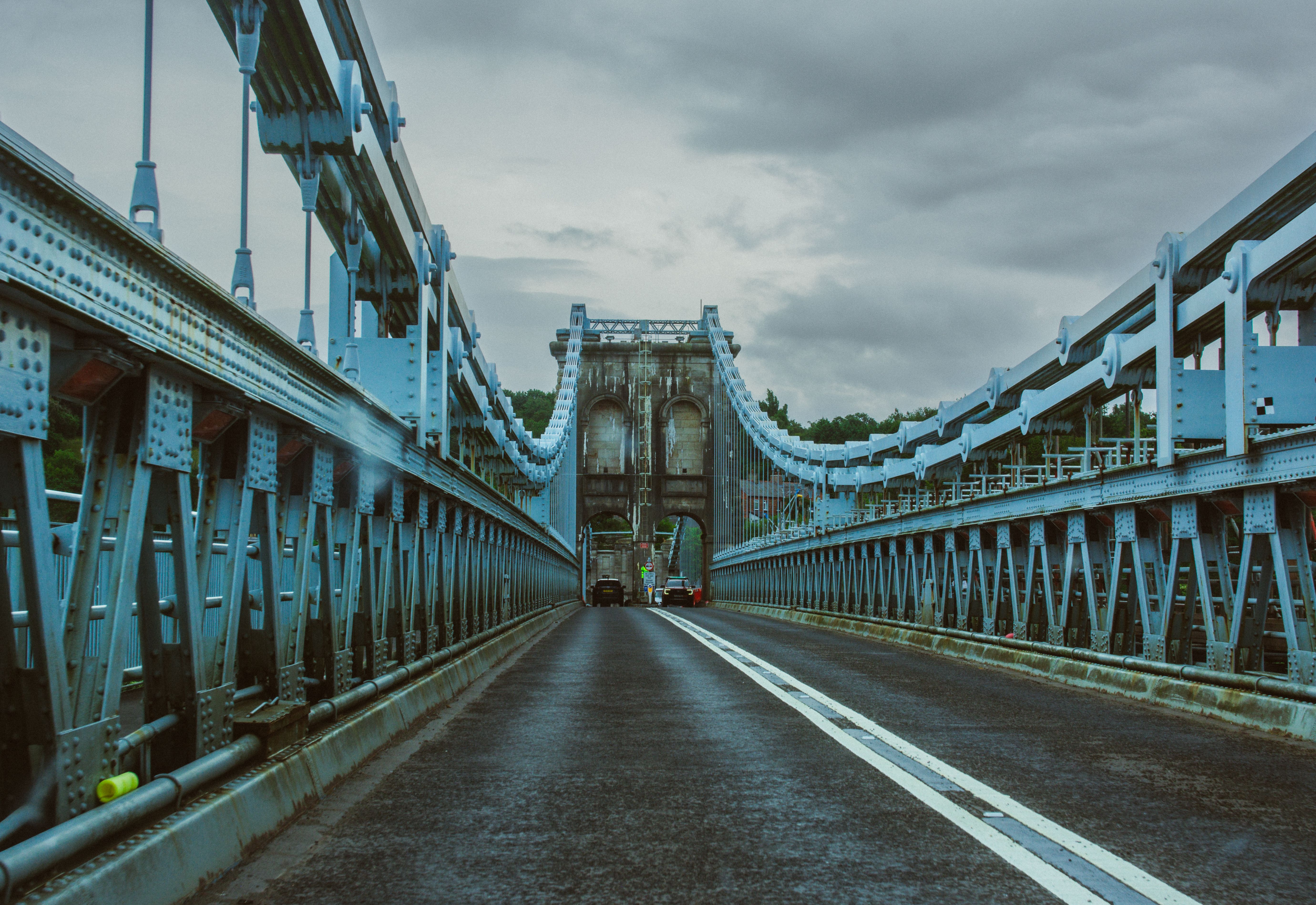 Dramatic view of the historic Menai Suspension Bridge in Wales, under overcast skies, emphasizing its architectural elegance.