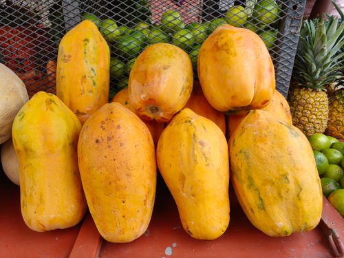 Free Vibrant display of ripe papayas, pineapples, and limes at a bustling outdoor market. Stock Photo