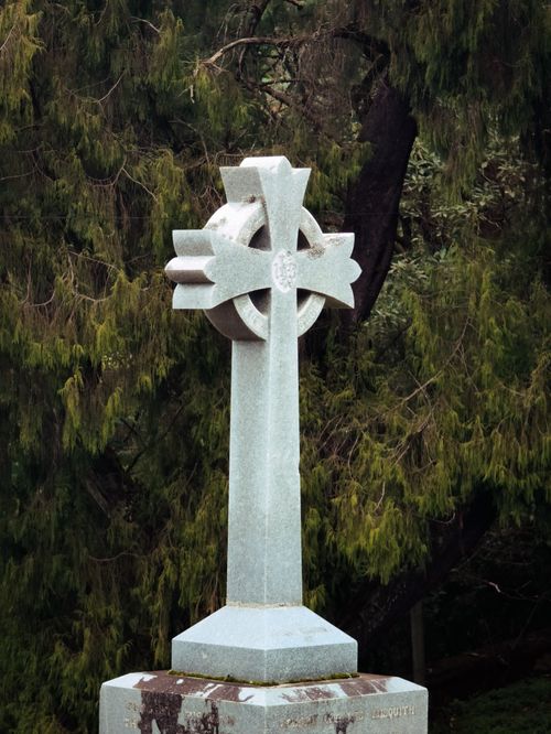 Free A stone Celtic cross monument stands in a lush, green cemetery setting. Stock Photo