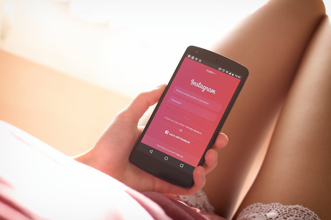 An image of a woman holding a phone with the Instagram login screen.