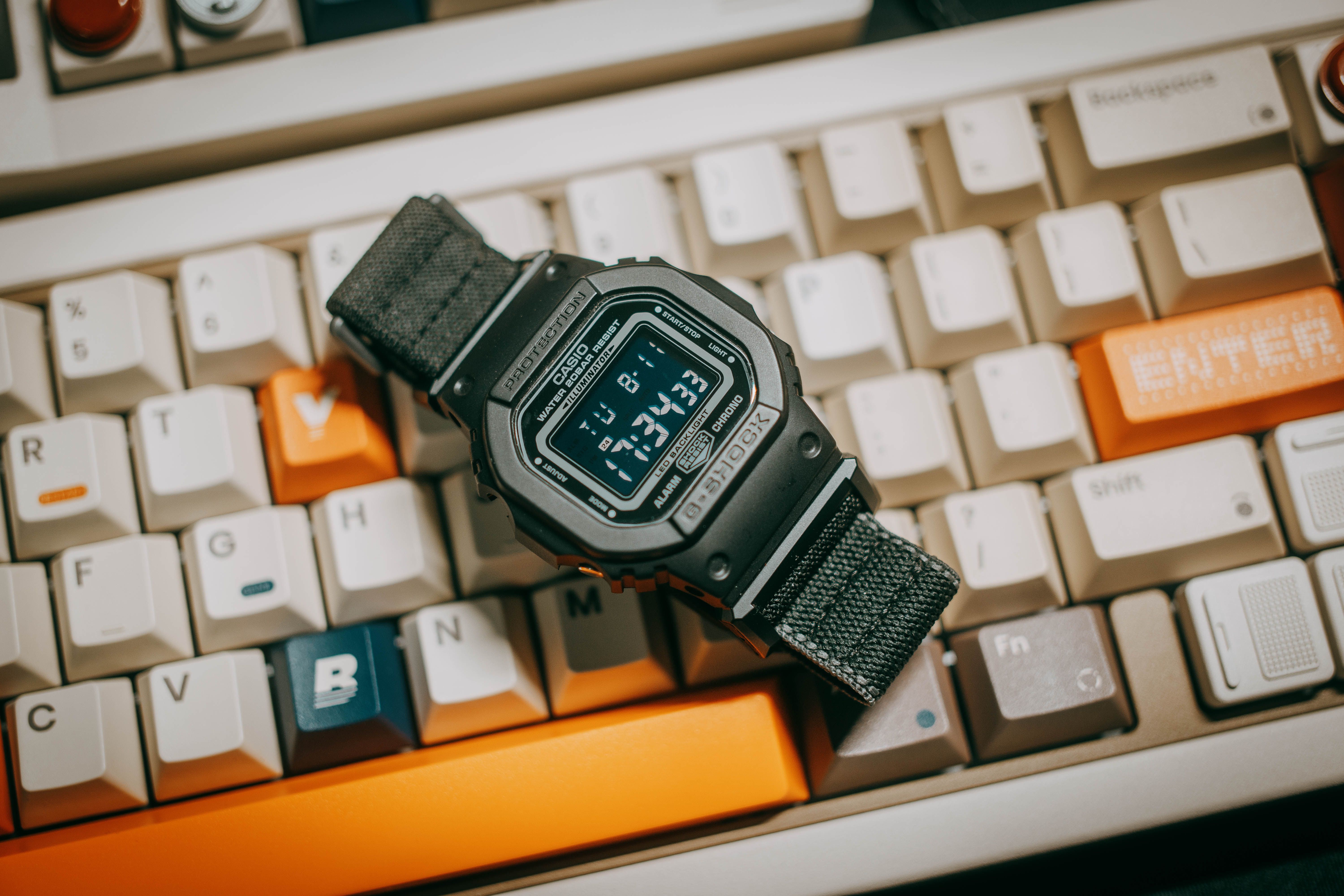 Close-up of a black digital watch resting on a mechanical keyboard with colorful keys.