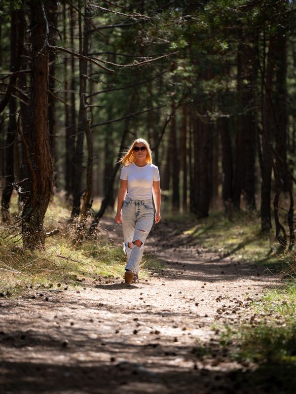 Woman walking a path through a sunlit pine forest — photo by Vilnis Husko on Pexels