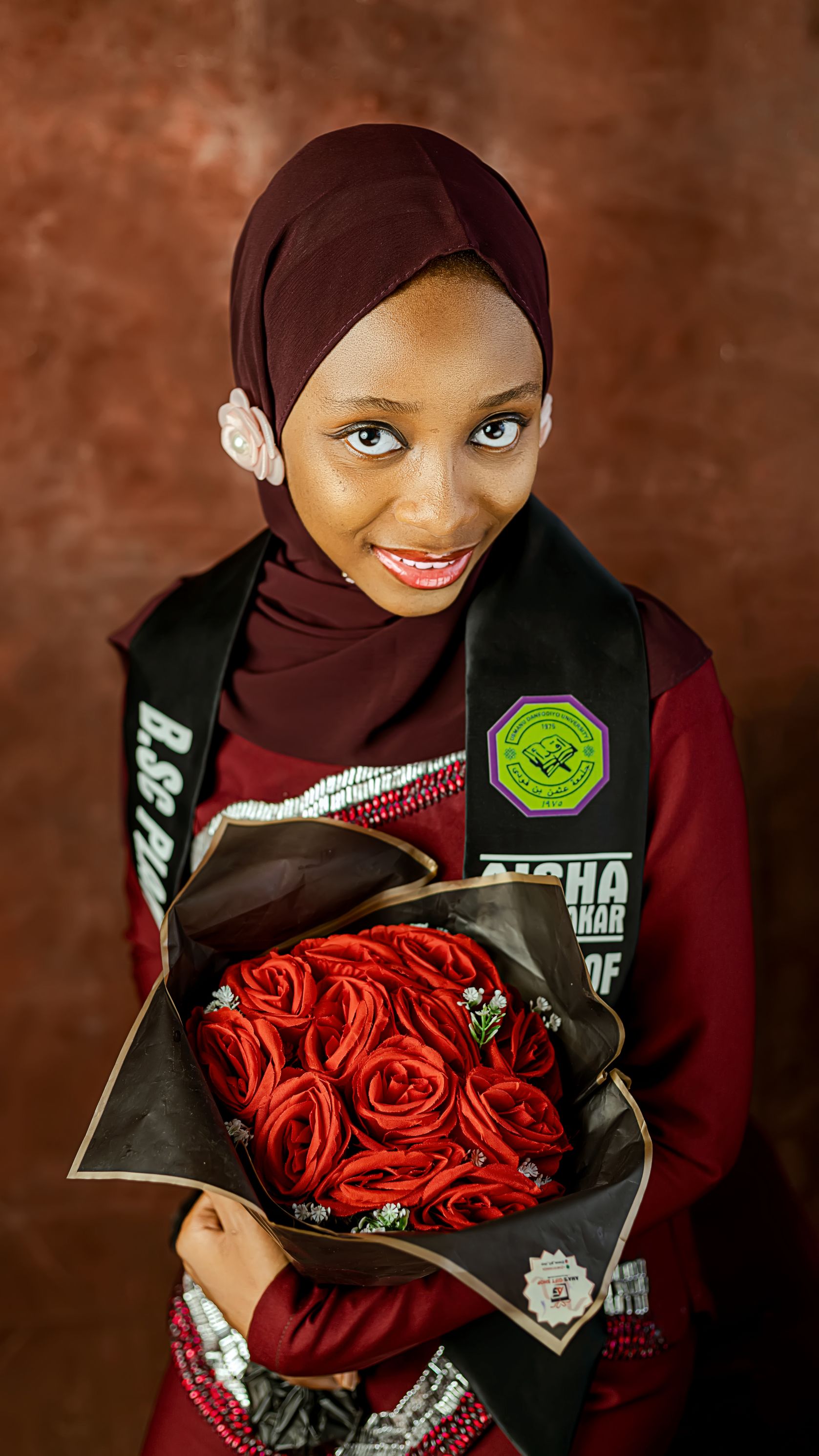 Young woman in graduation attire holding a bouquet of red roses with a joyful expression.