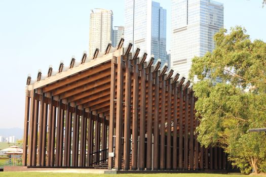 Contemporary wooden pavilion structure set against a backdrop of skyscrapers, capturing urban and architectural harmony.