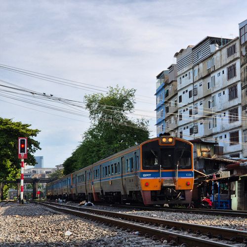 Free A commuter train travels through a bustling Bangkok neighborhood on a sunny day, showcasing urban life. Stock Photo