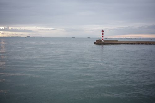 Free Peaceful coastal scene with a red and white lighthouse by calm waters at dusk. Stock Photo