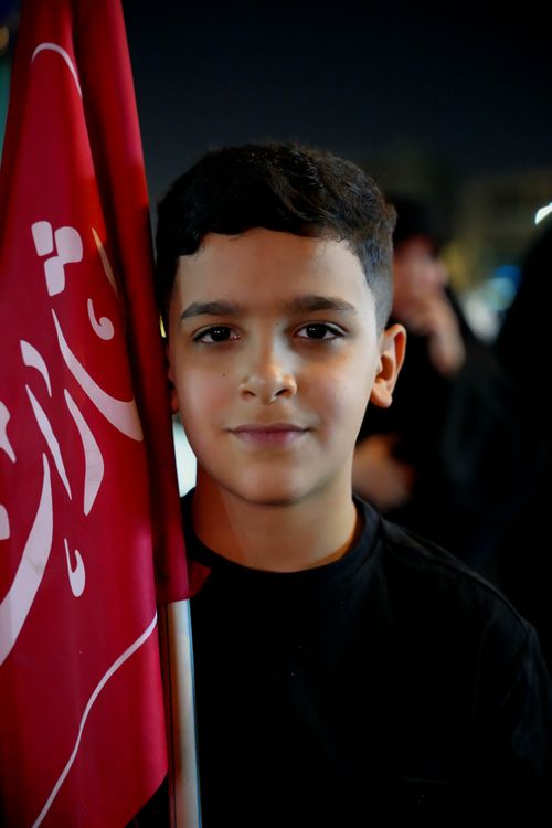 Free Portrait of a young boy holding a red flag during a night event in Karbala, Iraq. Stock Photo