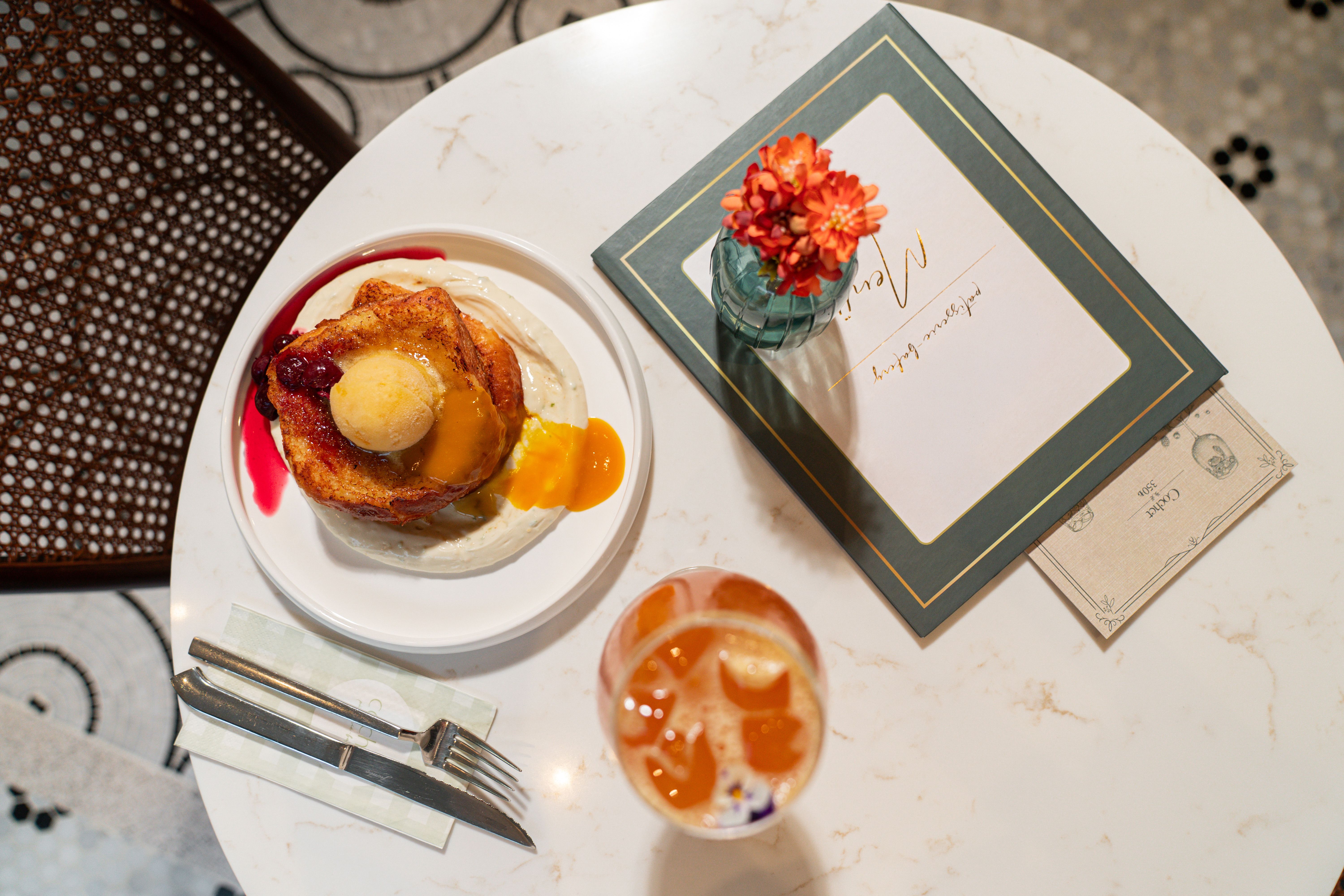 Overhead view of a delectable French toast breakfast with a menu and floral decoration on a marble table.
