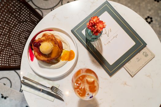 Overhead view of a delectable French toast breakfast with a menu and floral decoration on a marble table.