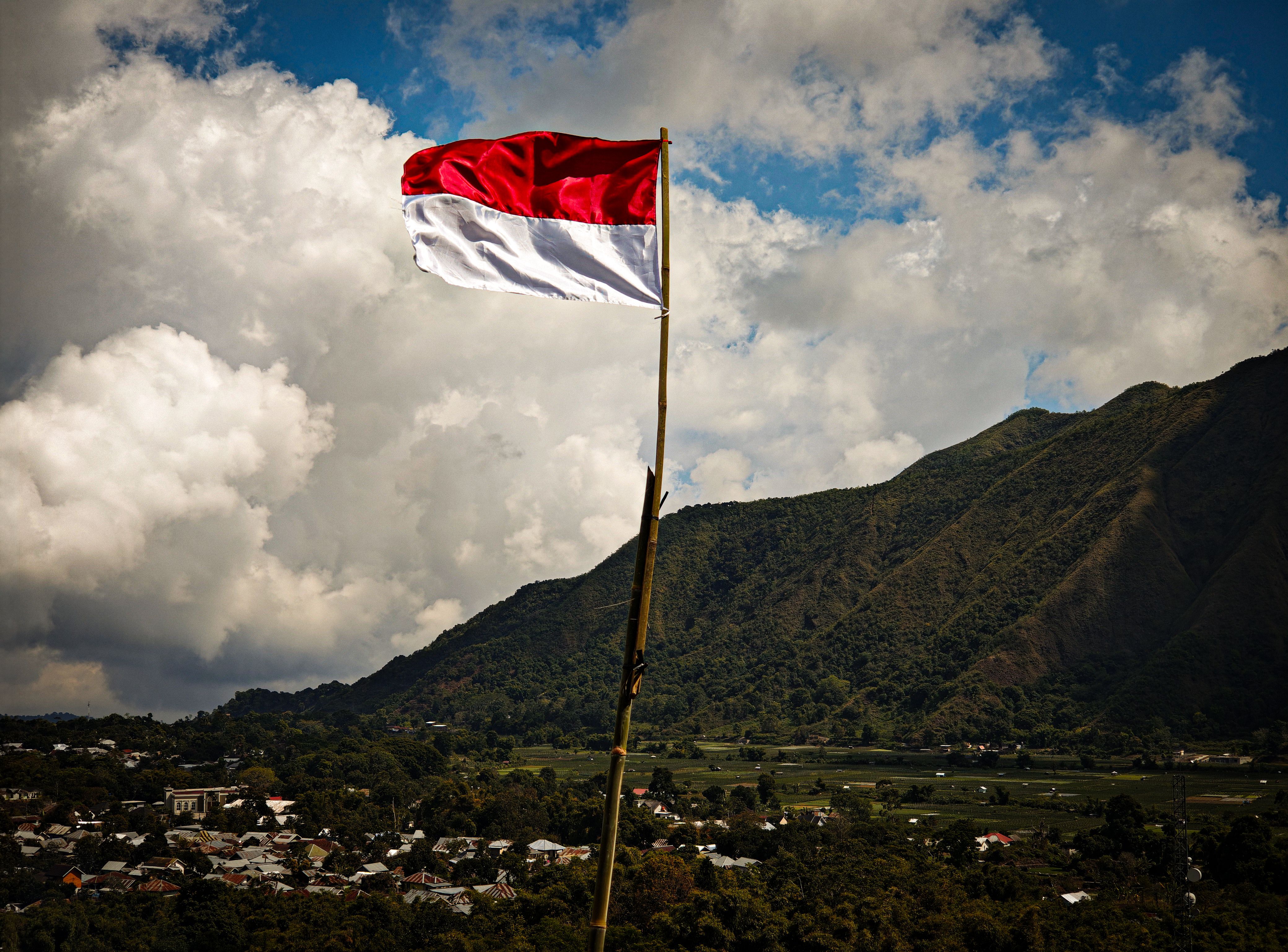 Bendera Indonesia berkibar di tengah pemandangan pegunungan yang indah di bawah awan yang dramatis.