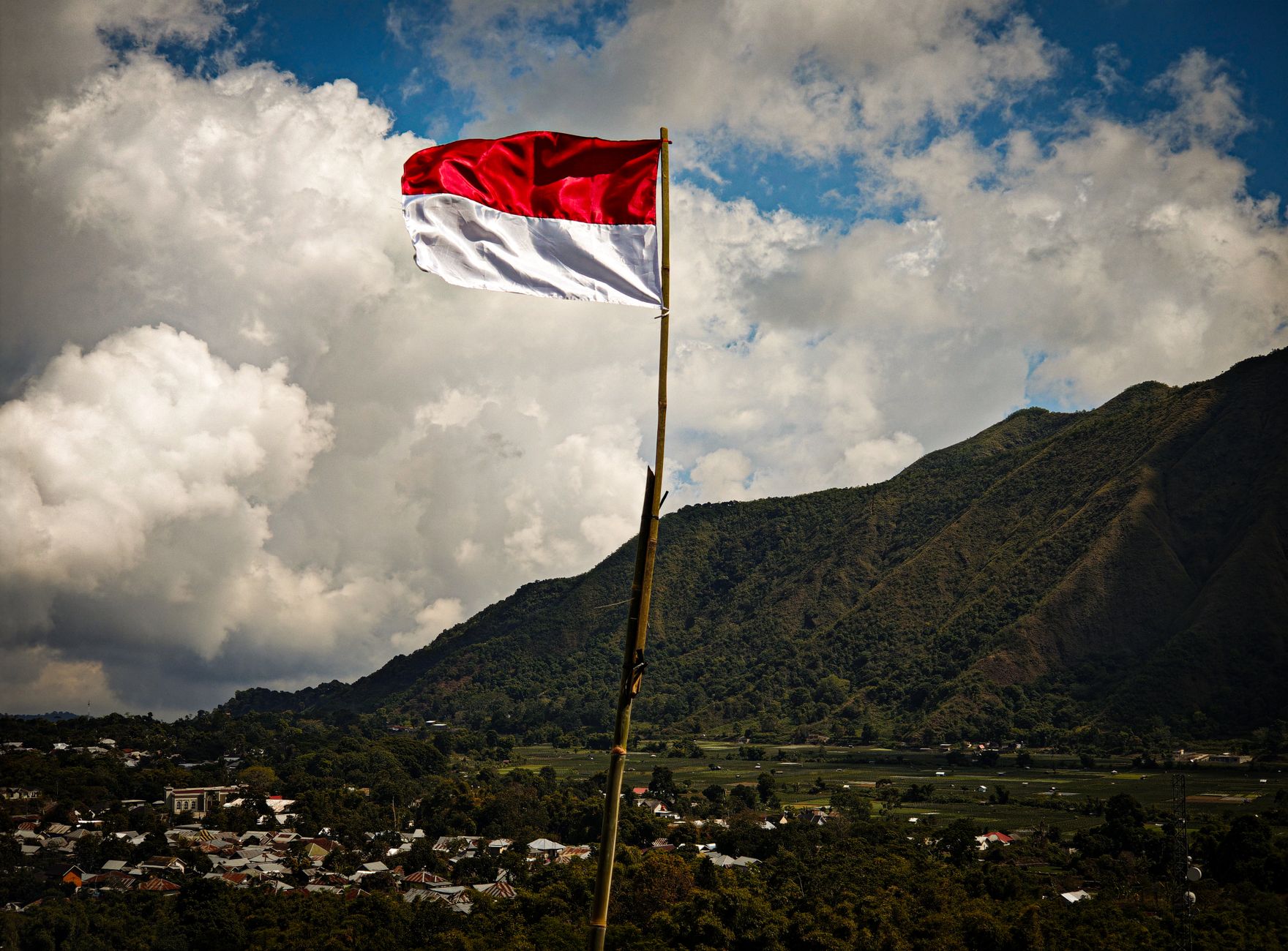 Bendera Indonesia berkibar di tengah pemandangan pegunungan yang indah di bawah awan yang dramatis.