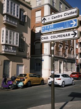 Street signs in a sunny Spanish city with cars and buildings.