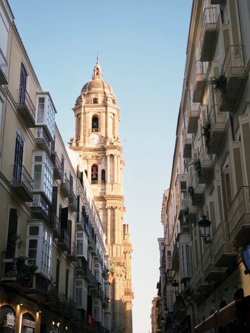 Free A stunning view of Malaga Cathedral's tower framed by classic European architecture at sunset. Stock Photo