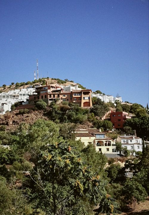 Free Charming hilltop villas under a clear blue sky, surrounded by lush greenery. Stock Photo
