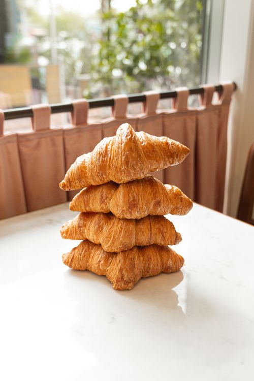 Free A stack of freshly baked croissants placed on a marble table near a window. Stock Photo