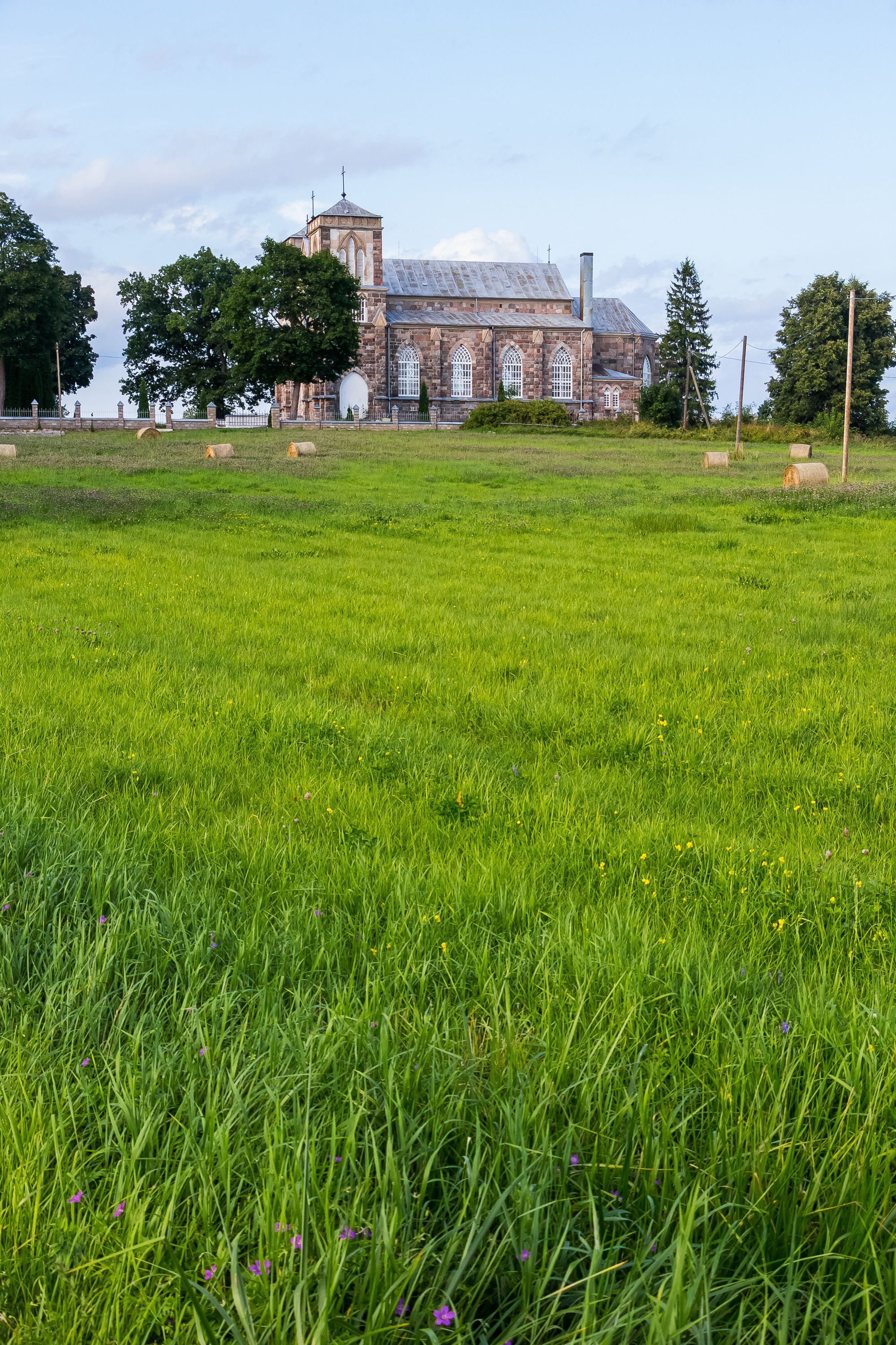 A tranquil view of a historic stone church surrounded by lush green pastures under a clear sky.