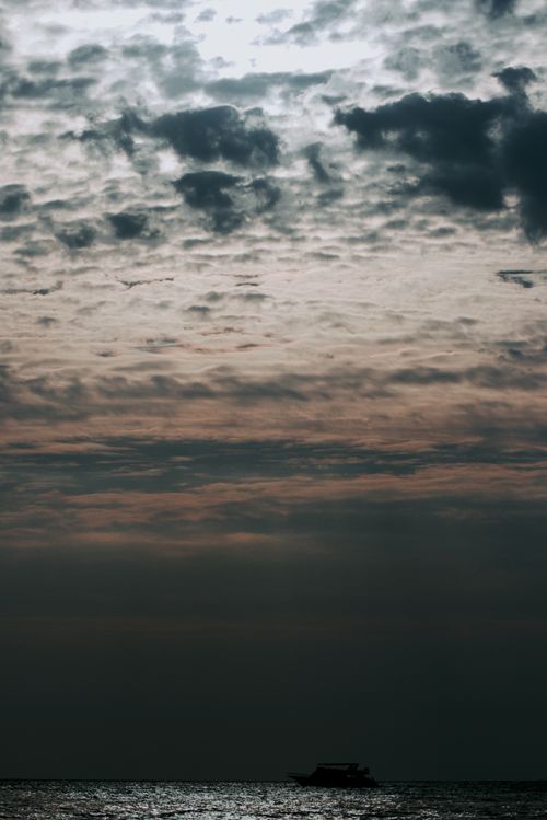 Free Dramatic twilight sky over ocean with a boat silhouette, creating a serene seascape. Stock Photo