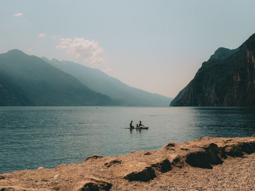 Free Canoeists paddle on tranquil Lake Garda surrounded by mountains in Italy. Stock Photo