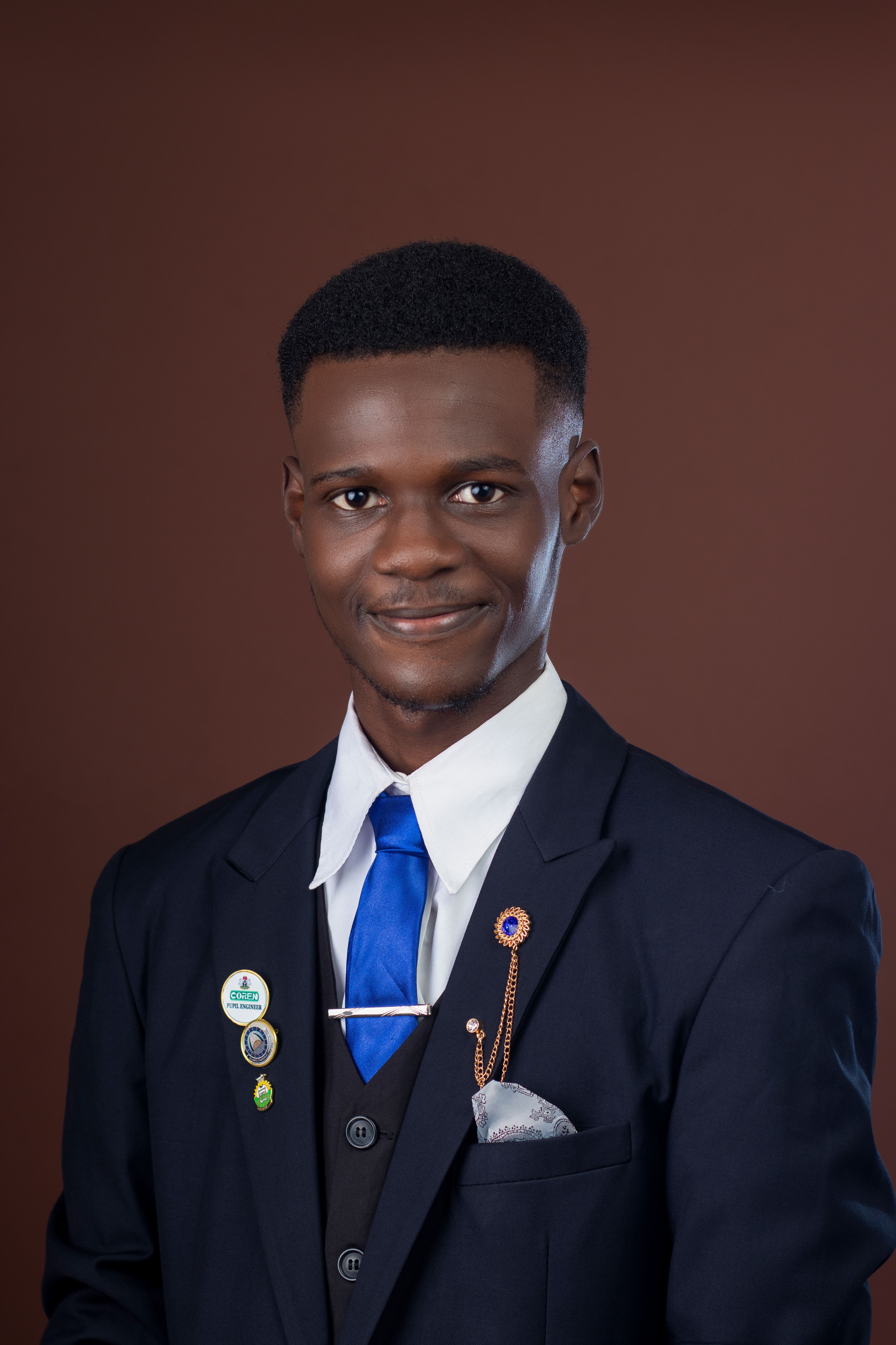 Portrait of a smiling young man in formal attire with a blue tie, set against a brown background.