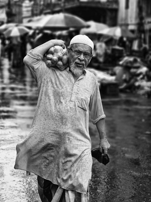 Free An elderly man carrying groceries through a rainy street market in Kolkata, India. Stock Photo